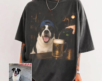 May include: A charcoal gray oversized t-shirt featuring a graphic print of a black and white dog wearing a blue baseball cap. The dog is sitting at a bar while a hand pours beer into a glass mug. A small inset photo shows the same dog.