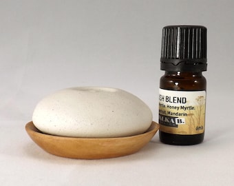 Könnte beinhalten: Ein weißer Diffusorstein aus Keramik mit einer Holzbasis und einer kleinen braunen Glasflasche mit ätherischem Öl. Das Etikett der Flasche lautet "Bush Blend Myrtle, Honey Myrtle, Fruit, Mandarin ALKA B. 6mls".