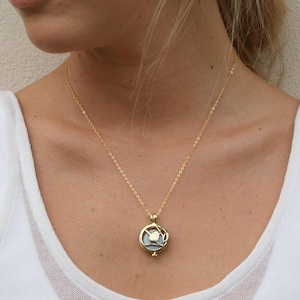 Puede incluir: Un collar de cadena dorada con un colgante redondo que presenta un delicado diseño de pájaro. El colgante tiene un inserto de vidrio o cristal transparente.