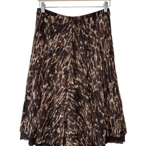 May include: A brown and tan patterned skirt hangs on a wooden hanger. The skirt has a flowing, A-line silhouette with a layered hem. The fabric features a repeating pattern of vertical brushstrokes in shades of brown and tan.