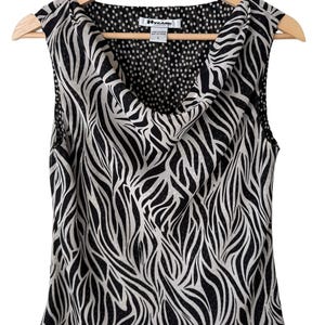 May include: Sleeveless top with a black and white zebra print design. The top features a cowl neck and is hanging on a wooden hanger. The interior lining of the cowl neck has a black and white polka dot pattern.