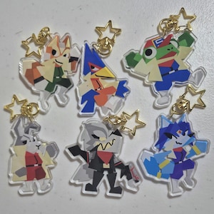 Puede incluir: Colección de seis llaveros acrílicos con personajes de la serie de videojuegos Star Fox. Cada llavero tiene un cierre dorado en forma de estrella. Los personajes incluyen a Fox, Falco, Slippy, Wolf, Krystal y Peppy.