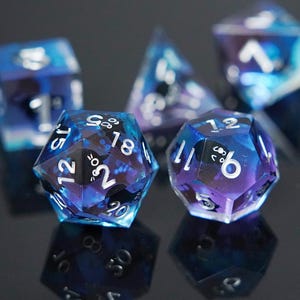 Peut inclure: Un ensemble de dés polyédriques avec un design galactique. Les dés sont un mélange de résine bleue, violette et transparente, avec des chiffres blancs. L'ensemble comprend un D20, D12, D10, D8 et D6, pour les jeux de rôle.
