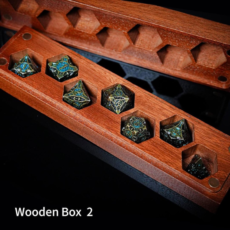 May include: A rectangular wooden box with hexagonal cutouts containing six multi-faceted metal dice. The dice feature an intricate dark bronze finish with blue enamel accents. The box has a matching wooden lid with hexagonal patterns. Text reads Wooden Box 2.