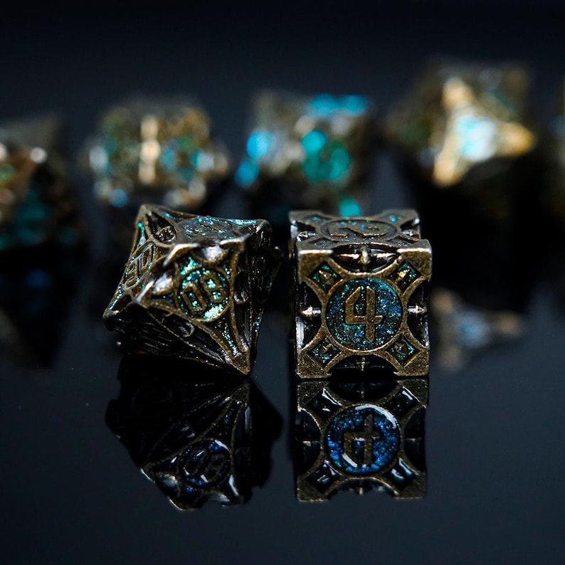 May include: Two multi-faceted metal dice with an antique bronze finish and recessed teal glitter enamel inlay. The cube-shaped die displays the number four, while the adjacent die shows the number eight. Both dice feature intricate geometric patterns.