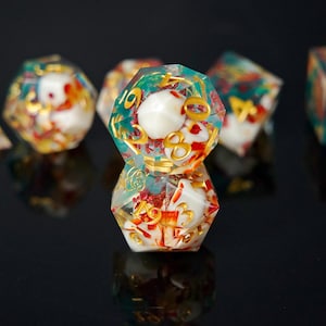 May include: Close-up of several polyhedral dice. The dice are clear with white, red, and gold accents. The numbers are gold. The dice have a teal and gold border. The dice are on a black surface.