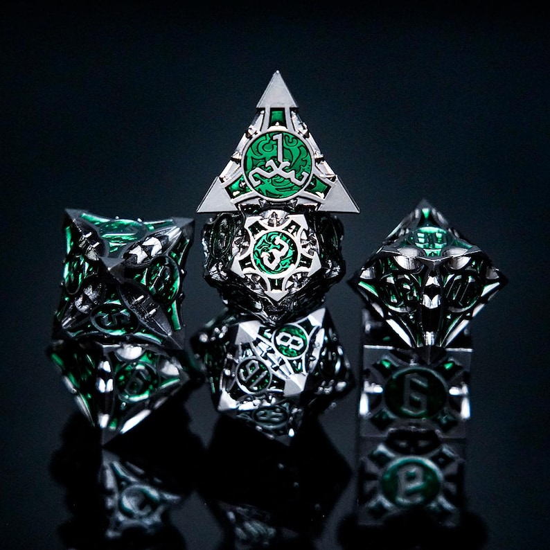 May include: A set of five multi-sided metal dice featuring a polished silver finish and intricate cut-out designs. Each die face contains a vibrant green enamel inlay with embossed numbers. The dice are arranged in a stacked and grouped formation.