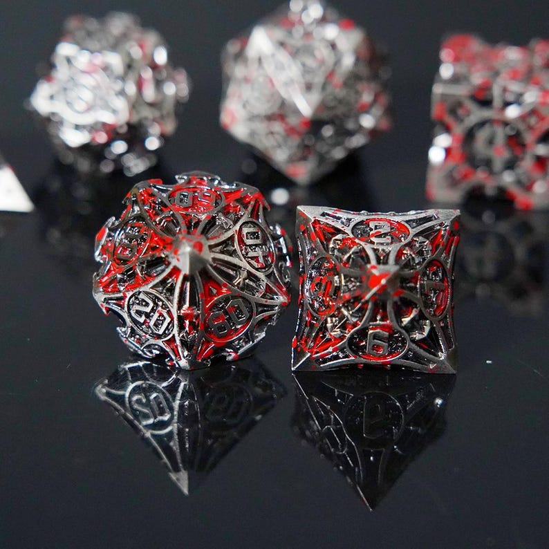 May include: A set of hollow metal polyhedral dice featuring a complex, openwork silver-toned frame with vibrant red enamel accents. The dice display clear numerical engravings on each face, with a multi-faceted design and sharp, pointed edges.