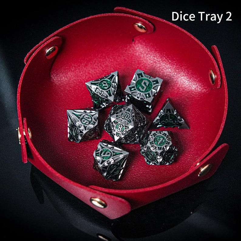 May include: A red, circular, collapsible tray with gold-coloured metal snaps, containing a set of seven intricate, silver-toned metal polyhedral dice with green enamel inlays. The text 'Dice Tray 2' is visible in the upper right corner.