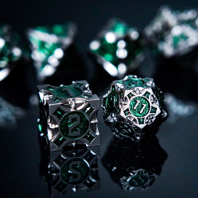 May include: A set of metal polyhedral dice featuring a silver-toned frame with intricate cutouts and deep green, translucent resin inserts. The dice display clear, embossed numbers, including a visible 2 on a cube and an 11 on a 20-sided die.