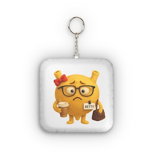Puede incluir: Un llavero amarillo con forma de personaje de dibujos animados con gafas, un lazo rojo y una etiqueta con el nombre "BETTY". El personaje sostiene una taza de café y un bolso marrón. El llavero tiene un anillo y una cadena plateados.