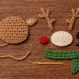 May include: A selection of crochet reindeer components: a brown head with ears, antlers, a red nose, a white oval, black eyes, a green scarf, and a yellow needle. All are arranged on a wooden surface.