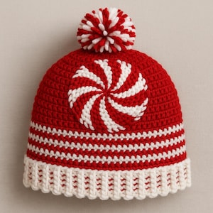 May include: A red and white crocheted beanie with a candy swirl design on the front. The hat features a white brim and a red and white pom-pom on top. The hat is a festive winter accessory.