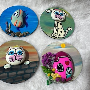 May include: Four hand-painted, round wooden coasters. Each coaster features a different design: a fish, a Dalmatian dog, a cat, and a pink house with a heart. The coasters are painted with bright colors and detailed designs.