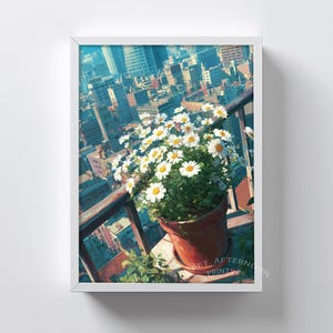May include: Framed print of a cityscape with a pot of daisies on a balcony. The daisies have white petals and yellow centres. The terracotta pot contrasts with the buildings under a blue sky.