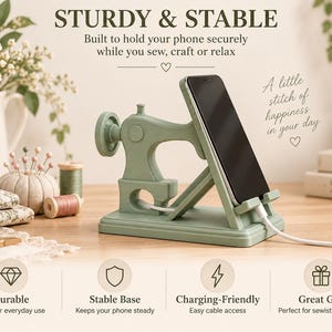 May include: A sage green phone stand shaped like a vintage sewing machine. The stand features a rectangular base, a side wheel, and a support arm holding a black smartphone with a white charging cable plugged into the bottom port.