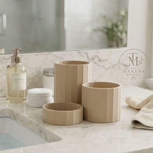 May include: A set of four beige bathroom accessories, including three cylindrical containers of varying heights and a small, round dish. The containers have vertical, ridged detailing. A soap dispenser and cotton pads are also visible.