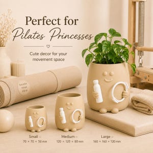 May include: Three beige ceramic planters with smiling faces, each holding a white bottle and ring. The planters are labelled small (70 x 70 x 50 mm), medium (120 x 120 x 80 mm), and large (160 x 160 x 120 mm). Text reads: Perfect for Pilates Princesses.