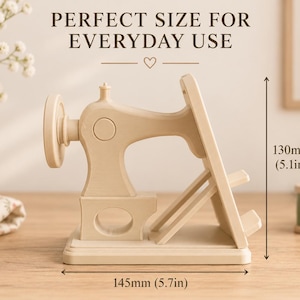 May include: A beige phone stand shaped like a vintage sewing machine. The stand measures 5.1 inches in height and 5.7 inches in width. The text PERFECT SIZE FOR EVERYDAY USE is visible above the object, which features a wheel and base.