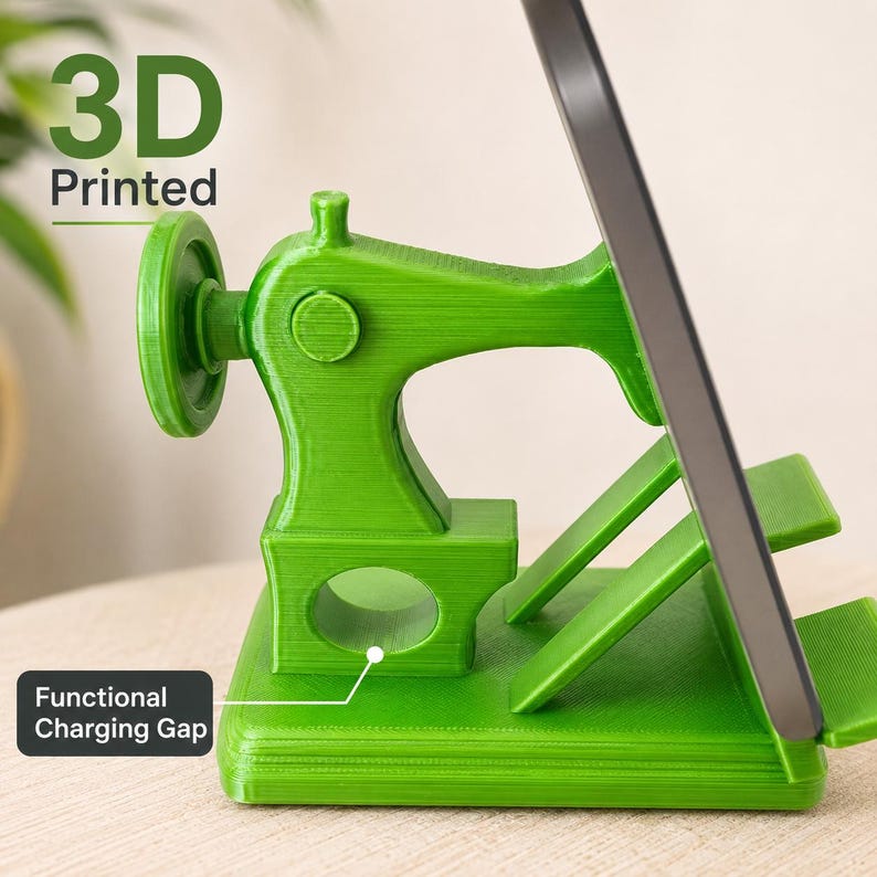 May include: A bright green 3D printed phone stand shaped like a vintage sewing machine. The stand features a side handwheel, a base with a functional charging gap, and an angled support for a mobile device. The text 3D Printed is visible.