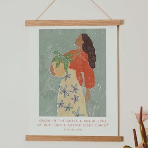 Peut inclure: Impression d'art représentant une femme tenant une plante en pot, vêtue d'un haut rouge et d'une jupe à fleurs. L'impression est encadrée dans un cadre en bois et comprend le texte "GROW IN THE GRACE & KNOWLEDGE OF OUR LORD & SAVIOR JESUS CHRIST 2 PETER 3:18."