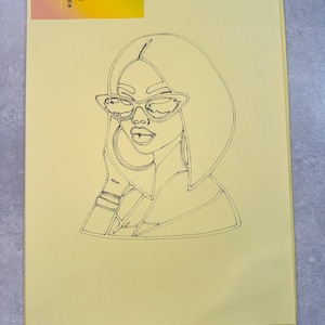 May include: A stack of pale yellow paper featuring a black line drawing of a woman in sunglasses. The drawing is on the front of the paper. A business card with the text "SANDRYLIX" is in the upper left corner.