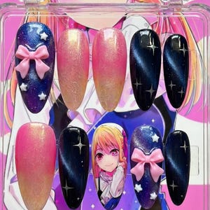 Peut inclure: Un ensemble de faux ongles dans un étui en plastique transparent. Les ongles présentent divers motifs, notamment un dégradé rose et or, bleu foncé avec des étoiles et un ongle avec un personnage d'anime. Certains ongles ont des nœuds roses.