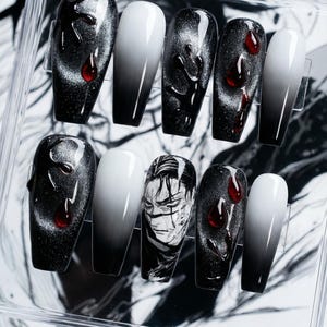 May include: A collection of ten coffin-shaped false nails in a clear case. Designs include black and silver glitter, white to black ombre, and a manga-style face. Some nails have red droplet accents. The nails are designed for cosmetic use.