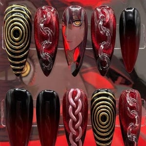 May include: A set of ten artificial nails in a clear plastic case. The nails feature various designs, including black and gold spirals, red and clear chain-like accents, a face, and ombre effects. The nails are almond-shaped.