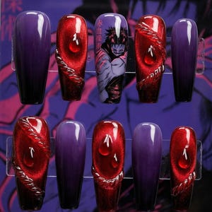 Pode incluir: Um conjunto de dez unhas artificiais em uma caixa de plástico transparente. As unhas apresentam uma mistura de designs, incluindo roxo sólido, vermelho com detalhes de gotas de água e uma ilustração de personagem. As unhas são em forma de caixão.