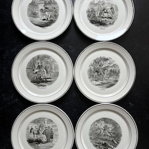 May include: A set of six white ceramic plates with a thin black rim. Each plate features a unique black and white circular illustration depicting historical scenes with horses and riders, labeled with the names ESPAGNE, HONGRIE, ANGLETERRE, FRANCE, TURQUIE, and AFRIQUE.