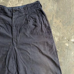 May include: Close-up of dark navy blue shorts. The shorts have a button closure and pleats at the waist. The fabric appears to be a soft, woven material. The shorts are slightly wrinkled, suggesting they are made of a natural fiber.