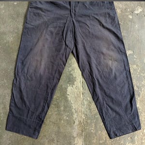 May include: Dark navy blue pants with a straight leg design. The pants have a button and zipper closure at the waist and feature a faded appearance, suggesting wear. The fabric appears to be a durable material.
