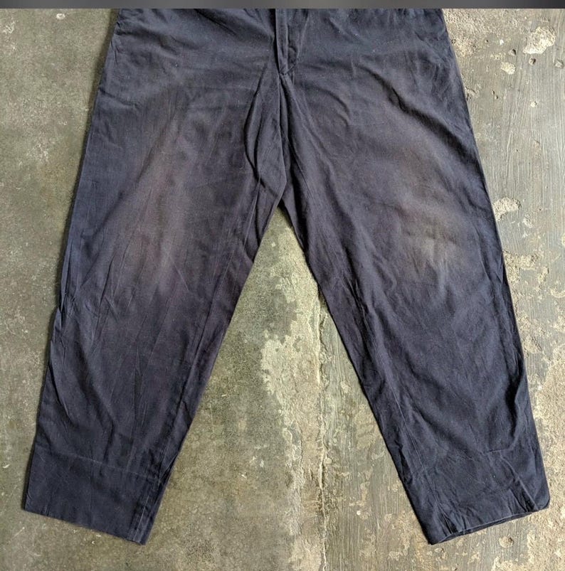 May include: Dark navy blue pants with a straight leg design. The pants have a button and zipper closure at the waist and feature a faded appearance, suggesting wear. The fabric appears to be a durable material.