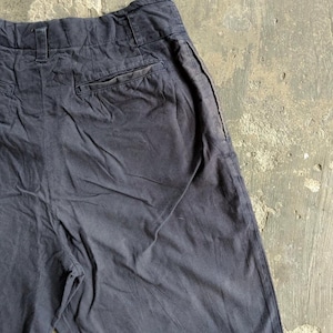 May include: Dark navy blue pants with a high waist and a back pocket. The pants have a relaxed fit and appear to be made of a soft, durable fabric. The pants are slightly wrinkled, suggesting they have been worn.