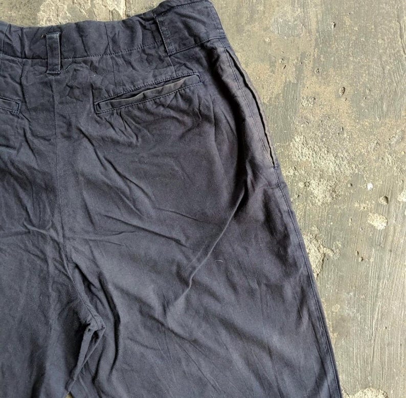 May include: Dark navy blue pants with a high waist and a back pocket. The pants have a relaxed fit and appear to be made of a soft, durable fabric. The pants are slightly wrinkled, suggesting they have been worn.