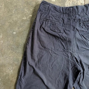 May include: Dark navy blue shorts with two back pockets and a button closure. The shorts are made of a slightly wrinkled fabric. The shorts are a casual style.