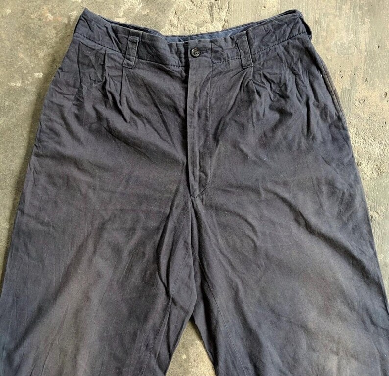 May include: Dark navy blue pants with a button closure and pleats at the waist. The pants have a relaxed fit and appear to be made of a soft, durable fabric. The pants are a solid color and have a slightly faded appearance.