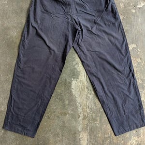May include: Dark navy blue pants with a relaxed fit. The pants have a straight leg design and appear to be made of a lightweight fabric. The garment is laid flat on a concrete surface, showcasing its full length and details.