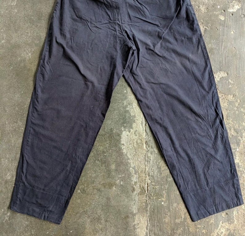 May include: Dark navy blue pants with a relaxed fit. The pants have a straight leg design and appear to be made of a lightweight fabric. The garment is laid flat on a concrete surface, showcasing its full length and details.