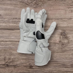 May include: A pair of white motorcycle gloves with protective padding on the knuckles and wrist. The gloves have black accents and a secure strap closure. The gloves are made of leather and are designed for safety and comfort.