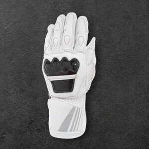 May include: White motorcycle gloves with black detailing. The gloves display the brand name "DAINESE" in black lettering on the knuckles and wrist. The gloves are made of leather and have protective padding for safety.