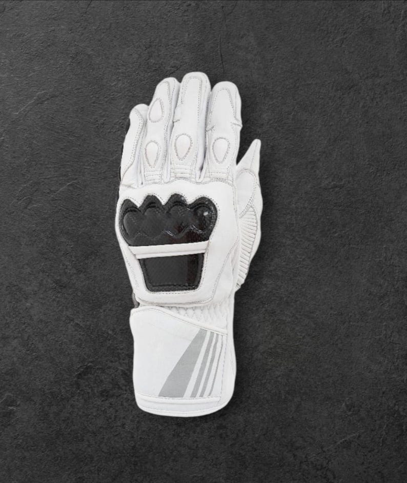 May include: White motorcycle gloves with black detailing. The gloves display the brand name "DAINESE" in black lettering on the knuckles and wrist. The gloves are made of leather and have protective padding for safety.