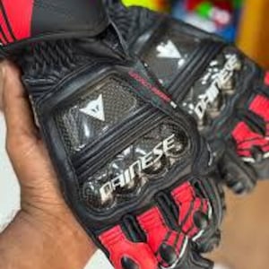Puede incluir: Guantes de moto negros y rojos con la marca "DAINESE". Los guantes tienen nudillos reforzados, dise&ntilde;o de fibra de carbono y una combinaci&oacute;n de cuero y materiales sint&eacute;ticos. Dise&ntilde;ados para protecci&oacute;n y rendimiento.