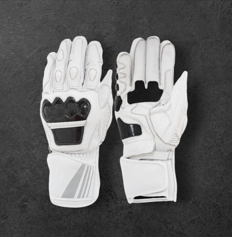 May include: White motorcycle gloves with black detailing. The gloves display the brand name "DAINESE" in black lettering on the knuckles and wrist. The gloves are made of leather and have protective padding for safety.