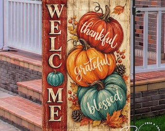 May include: A rectangular garden flag featuring a vertical red panel with the word WELCOME in white letters. The remaining area displays three pumpkins in orange, light orange, and teal, with the words thankful, grateful, and blessed in white.
