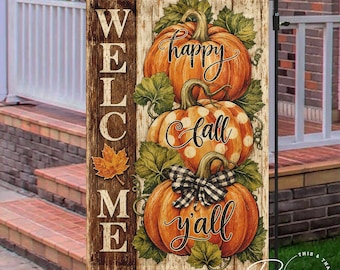 May include: A vertical garden flag featuring a wood-plank background with the text WELCOME in white. Three stacked orange pumpkins are decorated with green leaves, white polka dots on the middle pumpkin, and a black and white plaid bow.