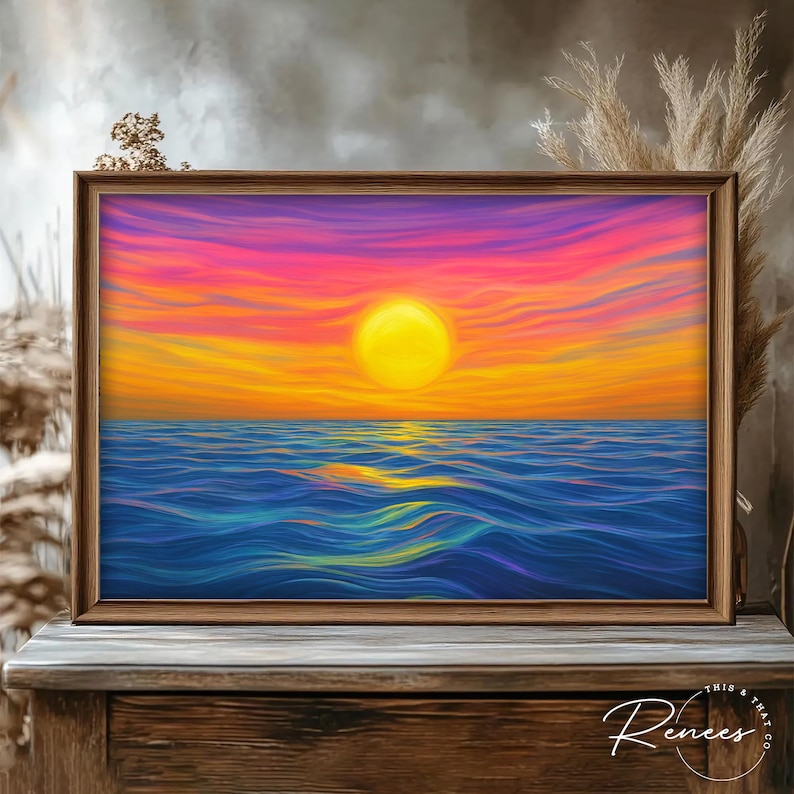 May include: A framed art print depicting a vibrant sunset over the ocean. The artwork features a large yellow sun, orange and pink sky, and blue water. The frame is made of wood. The text "This & That Co. Renees" is in the bottom right corner.