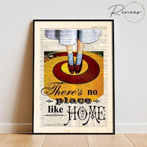 May include: Framed art print featuring a vintage book page background. The image depicts a scene from The Wizard of Oz, with ruby red shoes on a yellow brick road. Text reads "There's no place like HOME."