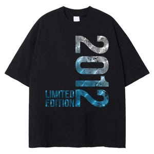 Pode incluir: T-shirt preto com o ano "2012" em um design prateado e azul desgastado. As palavras "LIMITED EDITION" são impressas abaixo do ano em azul. A camiseta tem mangas curtas e gola redonda.